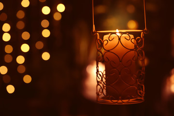 Fototapeta na wymiar Beautiful holder with burning candle in darkness against defocused lights