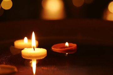 Small burning candles floating in plate with water, closeup
