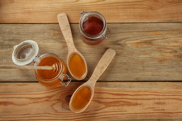 Jars and spoons with sweet honey on wooden background