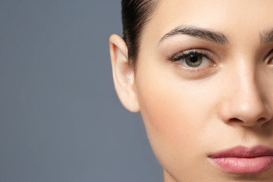Young woman with natural eyebrows on grey background, closeup