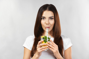 Beautiful young woman drinking lemonade on grey background