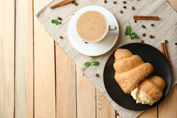 Delicious croissant with cup of coffee on wooden table