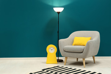 Trendy armchair with lamp near shaded spruce wall