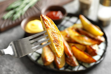 Fork with slice of tasty potato wedges, closeup