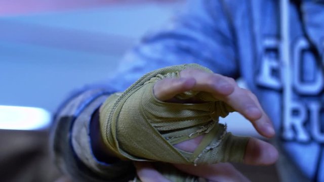 Boxer wrapping bandages on his hand before fight. Close up. Man ties his hands with a bandage