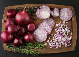 Cut and whole red onions with herbs on black background