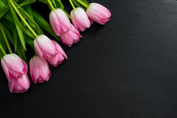 Border from bright pink tulips flowers on black wooden background. Selective focus. Place for text. Flat lay.