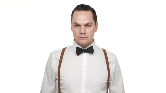 Portrait of caucasian man in white shirt straightening his black bow tie and being focused, over white background in studio. Concept of emotions