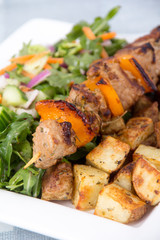 pork kebab skewer dish with potatoes and salad