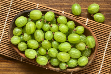 Raw gooseberries (lat. Ribes uva-crispa) in bowl, photographed overhead on dark wood with natural light (Selective Focus, Focus on the gooseberries on the top)