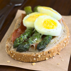 Überbackenes Vollkornbrot belegt mit Schinken, grünem Spargel, hartgekochtes Ei und geriebenem Käse, fotografiert mit natürlichem Licht (Selektiver Fokus auf die mittlere und rechte Spargelköpfe)