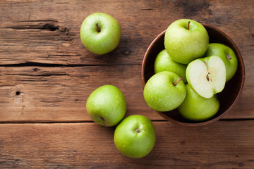 Ripe green apples in a wooden bowl on an old rustic table. Useful fruits on wooden background. Top view with copy space