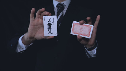A businessman or magician holds a playing card (joker) in a suit, a black background.