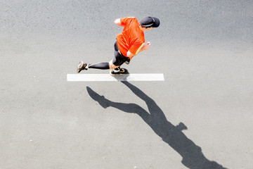 Single runner in sportswear against asphalt road with marking, top view