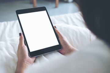 Mockup image of woman's hands holding black tablet pc with blank desktop white screen while sitting on a white bed