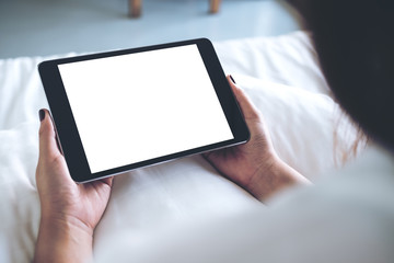 Mockup image of woman's hands holding black tablet pc with blank desktop white screen while sitting on a white bed