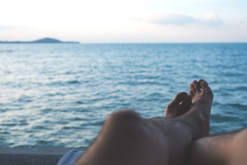 Closeup image of man's legs and foot while sitting by the sea with blue sky background