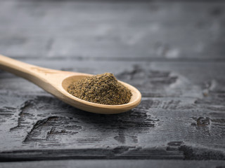 Ground black pepper in a spoon of light wood on a rustic table.