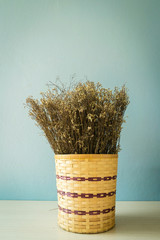 Dry grass flower and wood bucket on blue pastel color background.