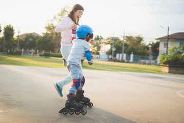 Obraz premium Asian mother helping her son to playing roller skate in the park