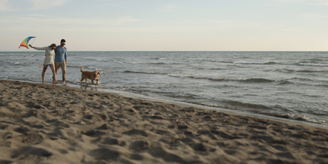 Fototapeta na wymiar couple with dog having fun on beach on autmun day