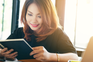 Asian stylish glasses woman designer wear black dress and red lips happiness reading a notebook in selective focus..