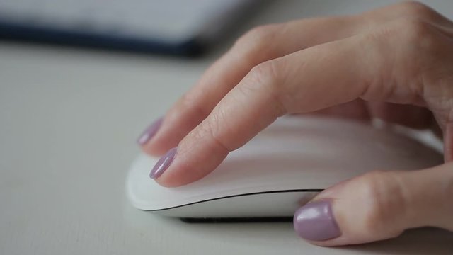 Woman is holding white stylish mouse by her hand, close up. Lady is working on computer and using brand-new device to cooperate with the machine. Female office worker is scrolling the pages by her