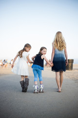 Two sisters helping their little sister roller skate on a sidewalk by the beach