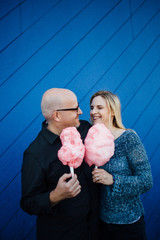 Man and a woman standing close to eachother in front of a blue wall holding pink cotton candy