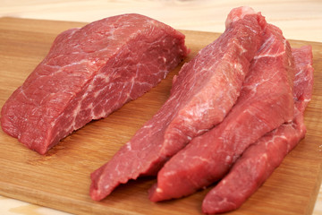 Raw beef piece and slices on wooden cutting board