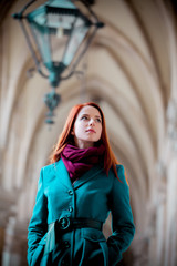 Young redhead girl in coat walking under archs