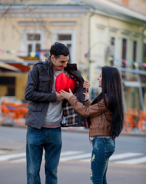 Young man giving a heart shape toy as a gift to young girl on the street