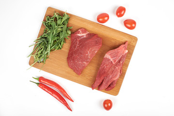 Sliced raw beef on cutting board and vegetables isolated on white background