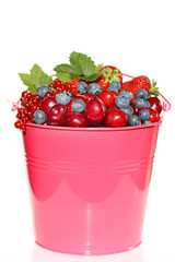 Berry season.bright pink bucket with berries of strawberries, blueberries, cherries, red currants  on white background. Harvest of berries. Delicious ripe berries in a pink bucket