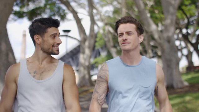 Two male friends walking and talking through a park