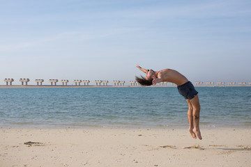 Young man doing somersault on the beach.