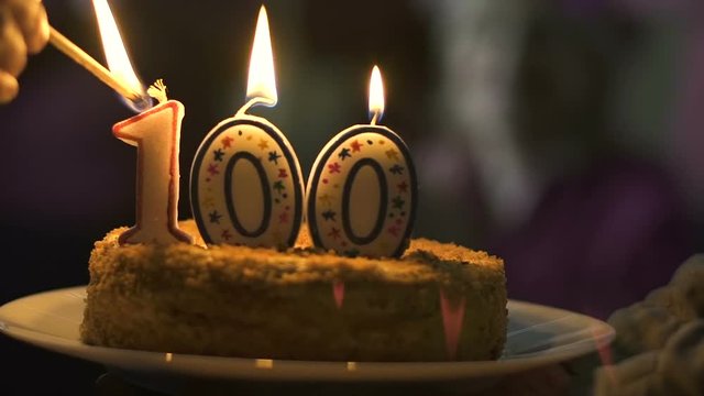 Hand lighting candles 100 on cake, company anniversary celebration, ceremony