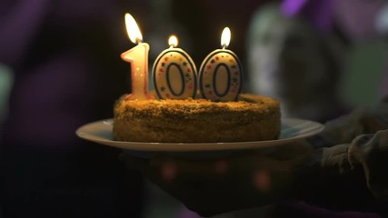 Friends giving birthday cake smiling senior woman, 100 anniversary celebration