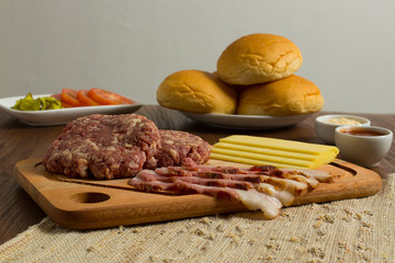 Ingredients for cooking burgers. Raw ground beef meat cutlets on wooden chopping board, cheese, bun,  over wooden background