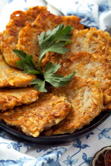 Potato latkes traditional jewish pancakes with sour cream, parsley, dry red pepper flakes and mint sauce. Background, white napkin with blue flowers. Hannukah celebration dish concept. Close up.
