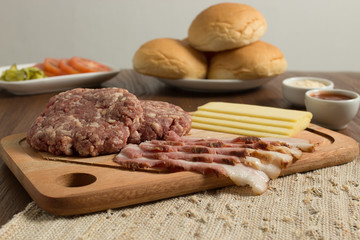 Ingredients for cooking burgers. Raw ground beef meat cutlets on wooden chopping board, cheese, bun,  over wooden background