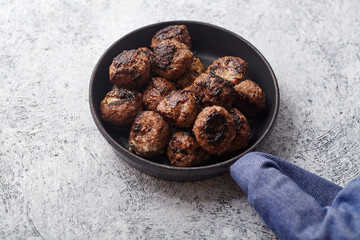 Traditional swedish beef meatballs served in one portion black cast iron pan, handle wrapped in blue towel. Textured background. Horizontal picture with copy space.