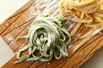 Two types of handmade italian tagliatelle pasta: classical one and green one with spinach on wooden cutting board