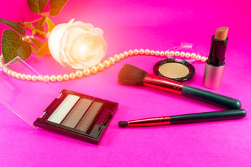 Obraz na płótnie Canvas Brushes and makeup cosmetics are placed on a pink background with pearl necklaces.