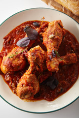 Chicken legs cooked in italian cacciatore style with tomato sauce and fresh basil on white table