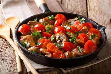 Delicious beef stew with tomatoes and greens close-up in a frying pan. horizontal