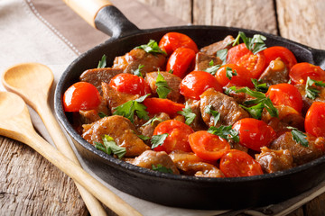 Spicy roast beef with tomatoes and greens close-up on a frying pan. horizontal