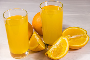 Glass of orange juice and fresh oranges on white wooden table