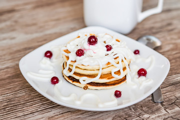Fresh baked pancakes for Breakfast in a white plate, decorated with sour cream and cranberries, close-up