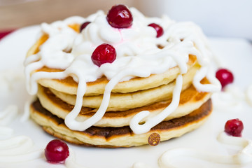 Fresh baked pancakes for Breakfast in a white plate, decorated with sour cream and cranberries, close-up